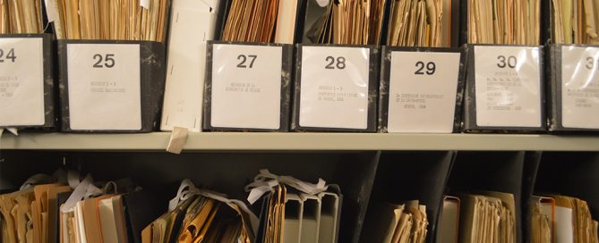 Shelves filled with numbered black folders containing organized paper documents and files.