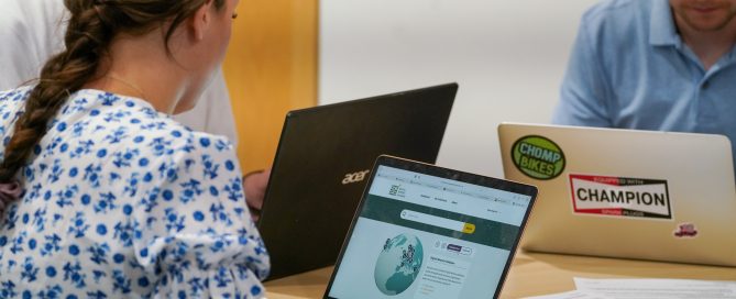 People working at a table with laptops, one of which displays the Digital Memory Database interface on the screen.