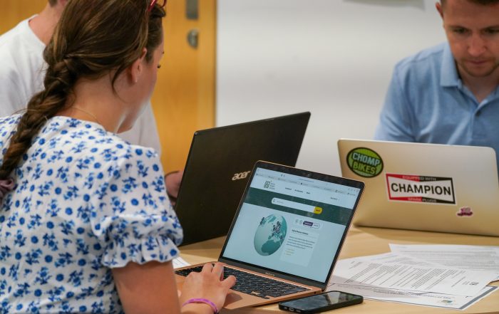 People working at a table with laptops, one of which displays the Digital Memory Database interface on the screen.
