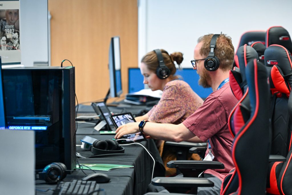 Two people wearing headphones use tablets and computers at a row of gaming chairs during a digital learning or gaming session.