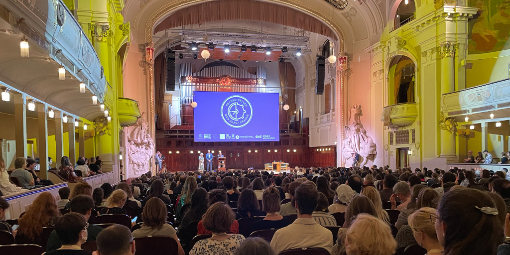 Large audience seated in an ornate concert hall with high ceilings and classical architecture, watching a presentation on a central stage with a large screen displaying the MSA 2025 logo.